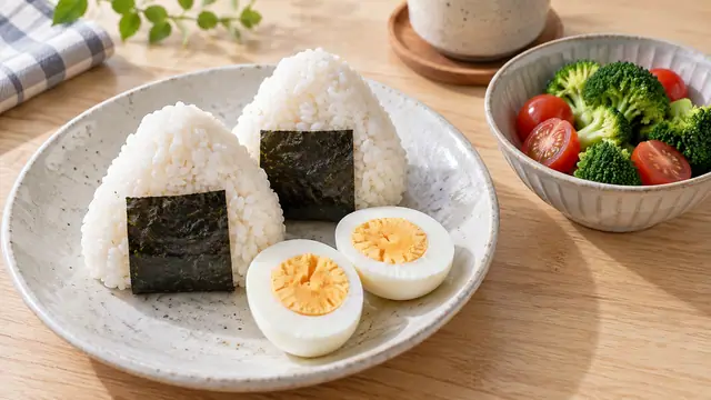 おにぎり2個にゆで卵と野菜の小鉢を添えた昼食のイメージ。特定商品や計量した分量を示す写真ではありません